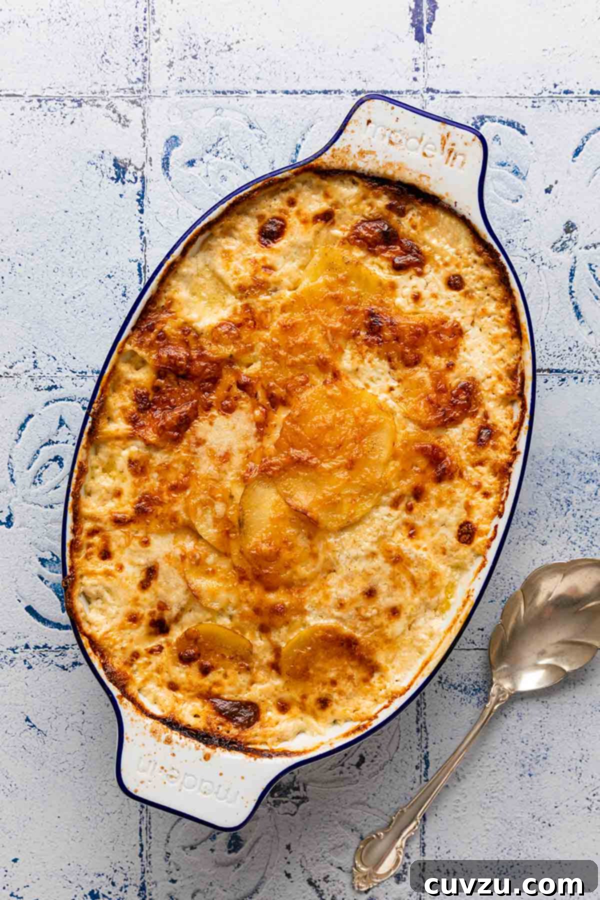 An inviting oval casserole dish filled with golden-brown potatoes dauphinoise, with a silver serving spoon resting gracefully beside it on a dark surface.