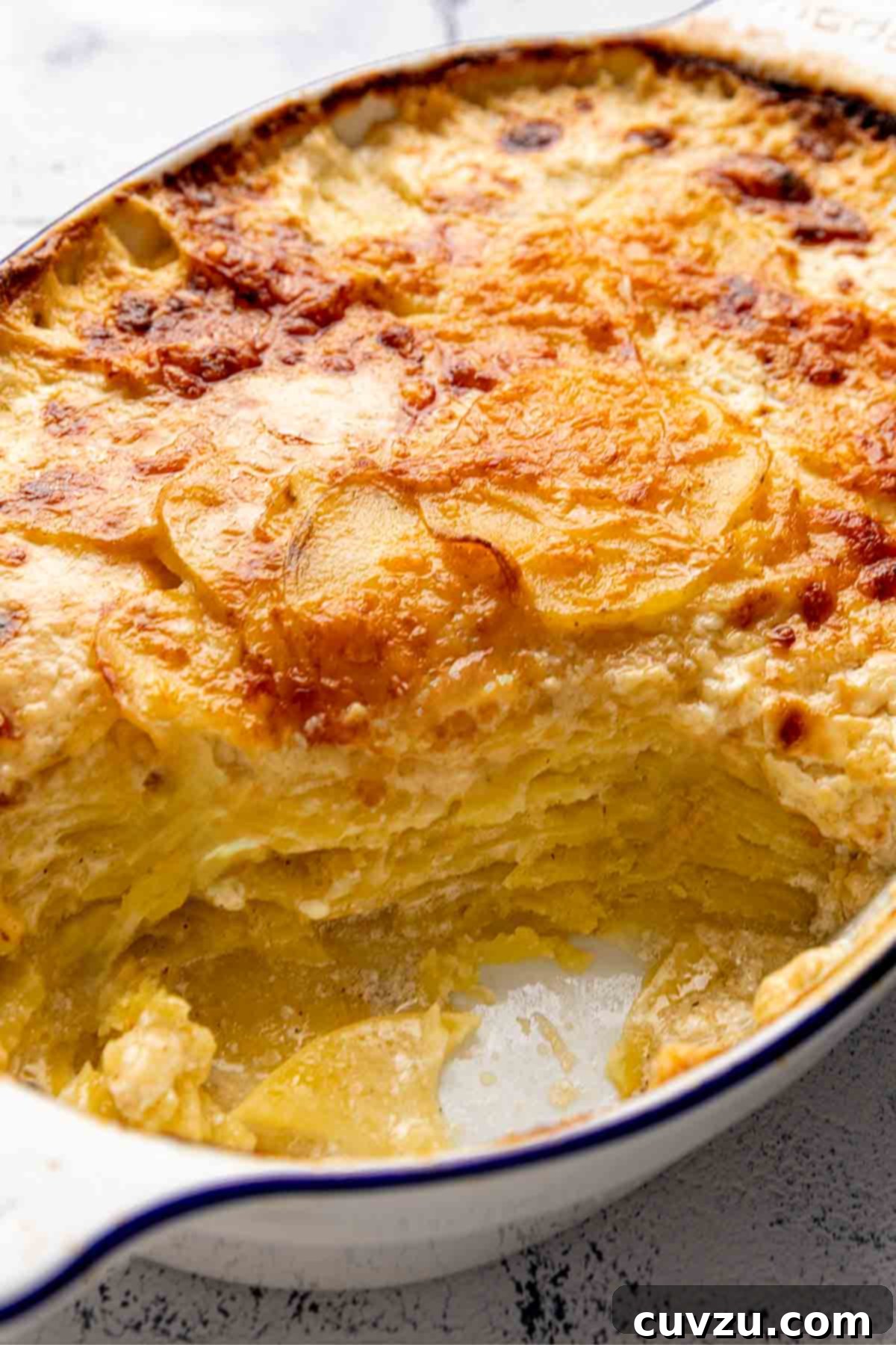 An oval casserole dish filled with perfectly cheesy, browned, and bubbly potatoes dauphinoise, fresh from the oven, invitingly delicious.