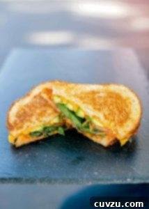 A delightful veggie grilled cheese sandwich, sliced in half and presented on a platter, showcasing its colorful vegetable layers and melted cheese.