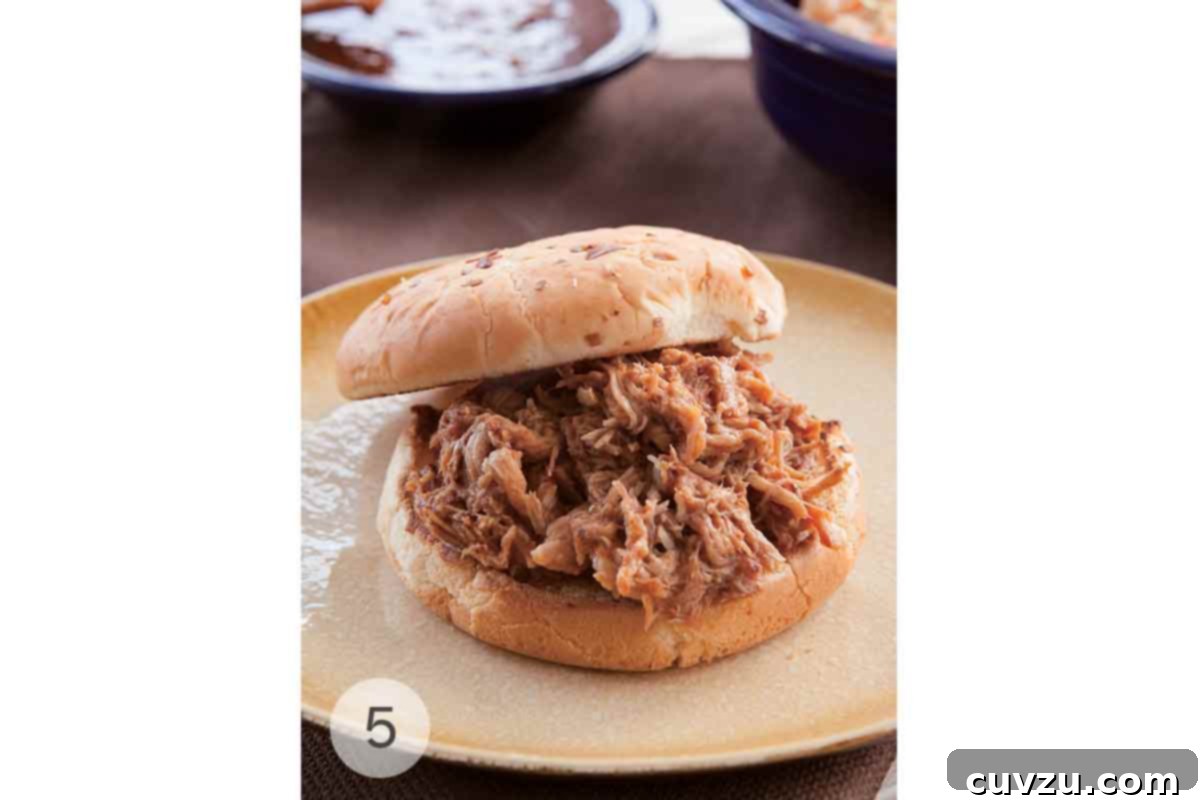 The Ultimate Slow Cooker Pulled Pork 4 Slow cooker pulled pork piled on a bun on a plate.
