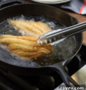 Southern fried catfish being fried in a cast-iron skillet, ready to be served golden and crispy.