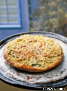 A cooked leftover pasta frittata on a round metal pan, garnished with herbs.