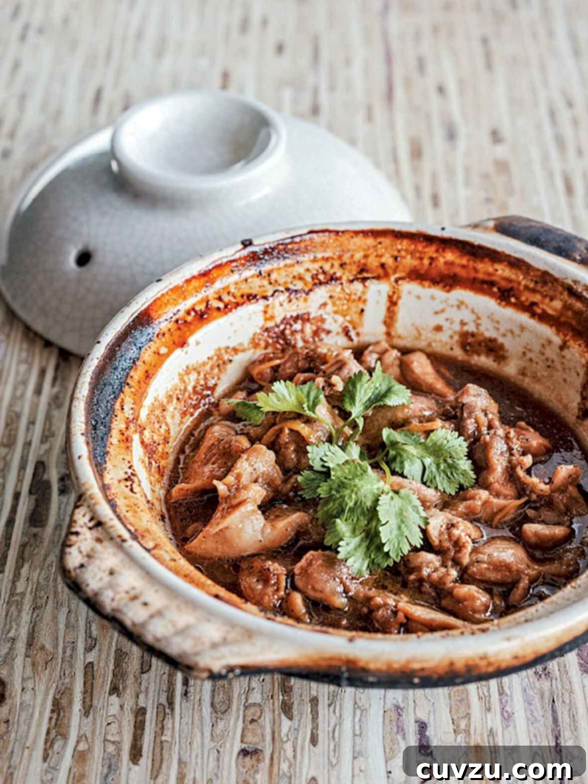 Golden Vietnamese Caramel Chicken 2 Clay pot filled with Vietnamese caramel chicken pieces and cilantro on a wooden table. A classic Vietnamese dish, Ga Kho, perfect for a flavorful weeknight dinner.