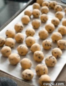 Balls of frozen chocolate chip cookie dough on a parchment-lined baking sheet.