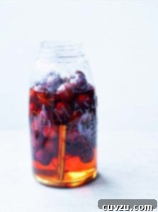 A mason jar mostly filled with pickled cherries, pickling liquid, star anise, and a cinnamon stick.
