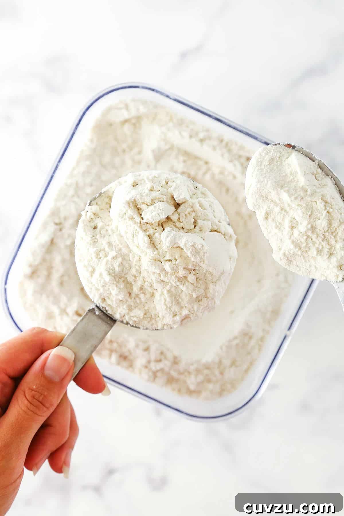 Properly Spooning Flour for Accurate Measurement Spoon fluffy flour into a measuring cup, demonstrating the first step of the 'spoon and level' method for accurate volume measurement.