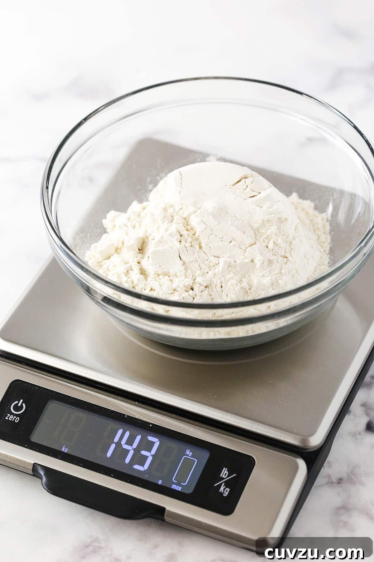 Direct Scoop: The Pitfall of Over-Measuring Flour A bowl of flour measured by the 'Direct Scoop' method, weighing 143 grams on a kitchen scale, illustrating significant over-measurement.