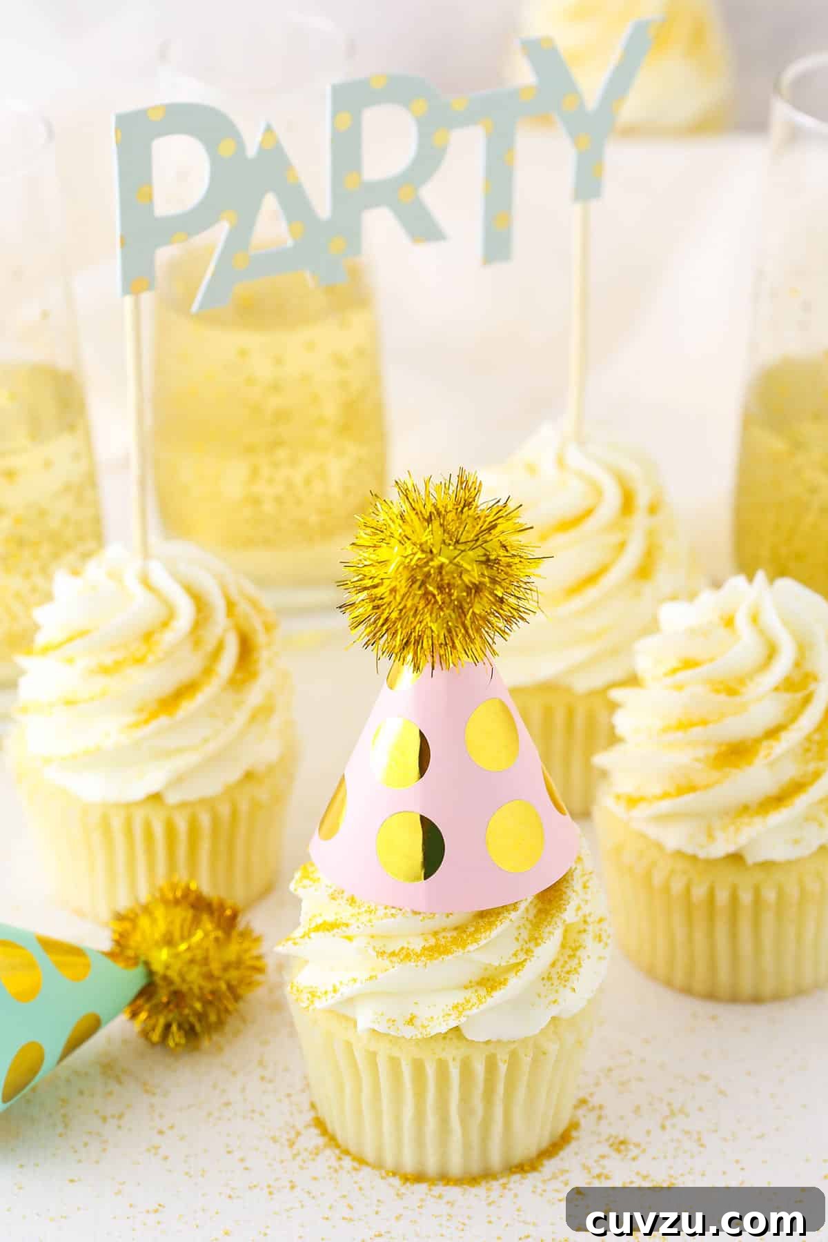 Enhanced Champagne Cupcake Recipe for Unrivaled Flavor and Texture Four Champagne Cupcakes decorated with buttercream frosting on a white table top with a filled champagne glasses in the background