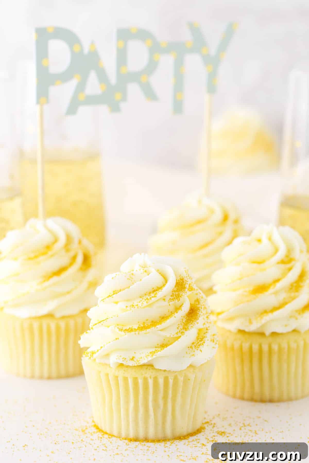 Champagne Buttercream for an Elegant Cupcake Topping Four Champagne Cupcakes decorated with buttercream frosting on a white table top with a filled champagne glass in the background