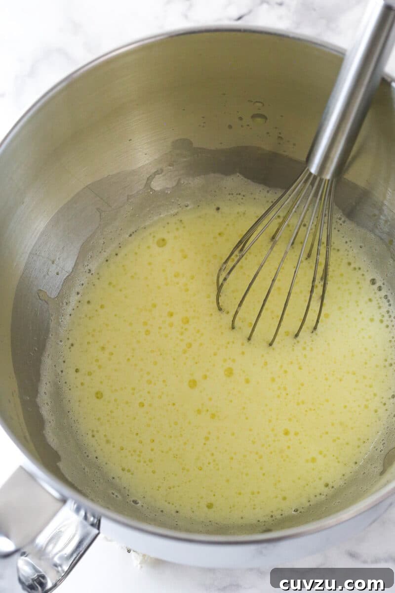 Cook the egg mixture gently to 160°F for perfect consistency. Close-up of the egg mixture being whisked over a double boiler, indicating the cooking process.
