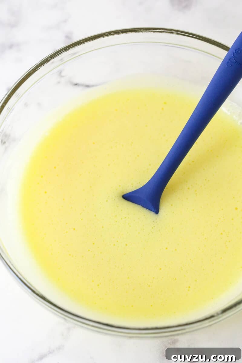 Stir melted gelatin into the prepared egg mixture until smooth. The melted gelatin being stirred into the warm, golden egg mixture in a glass bowl.