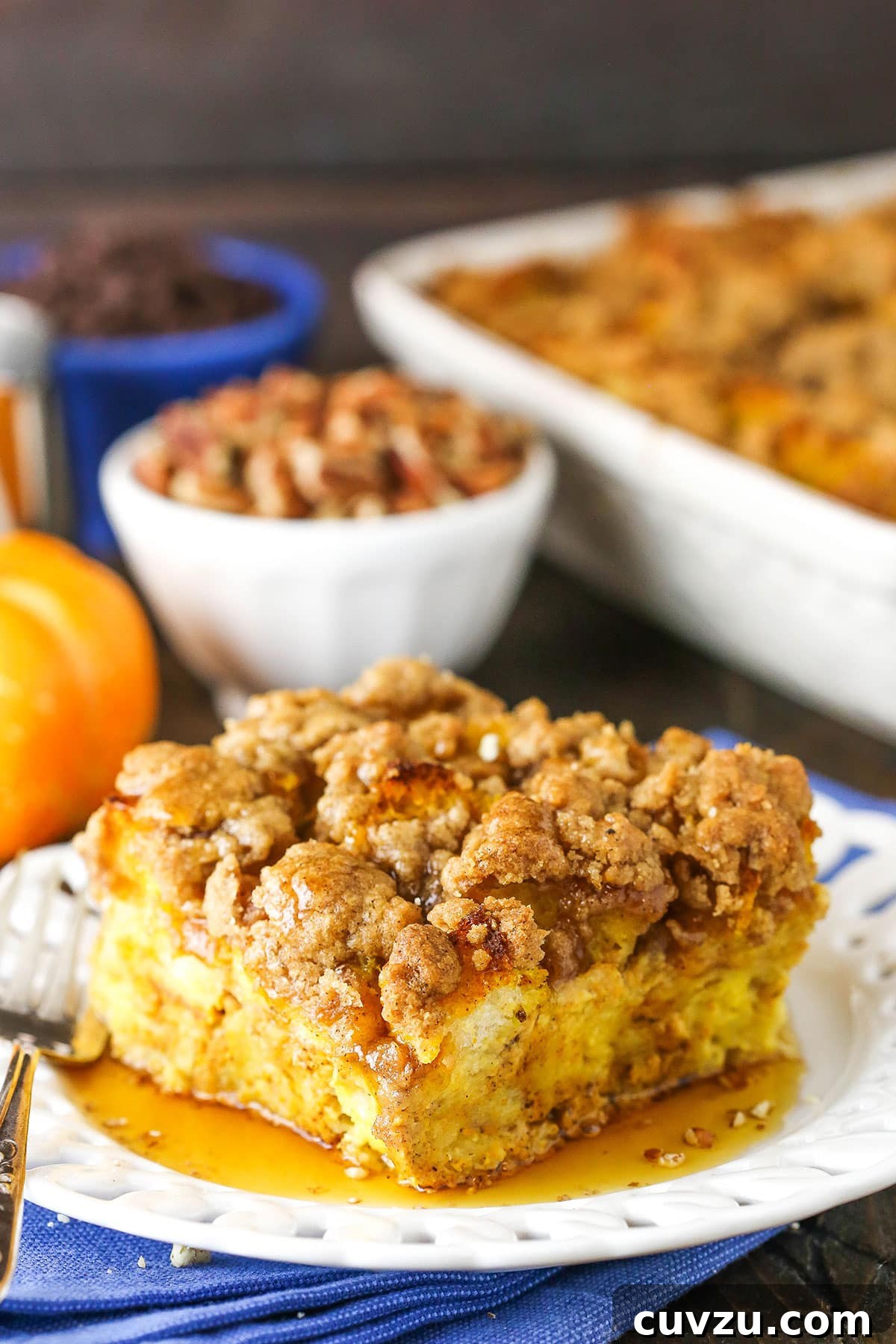 A perfect square of Pumpkin French Toast Casserole, ready to be enjoyed. Side view of a square serving of Pumpkin French Toast Casserole on a white plate with a fork, showing its rich, custardy interior.