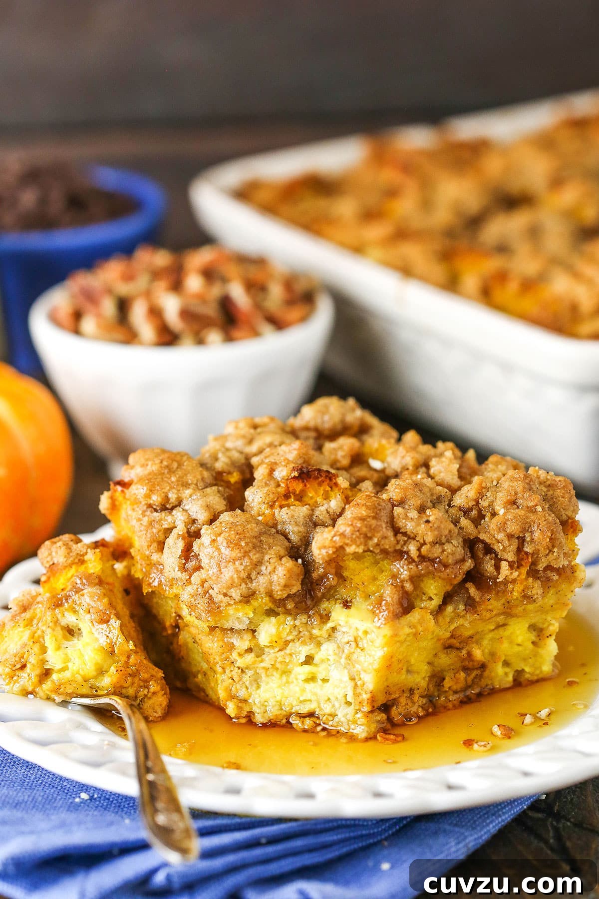Enjoying a delicious bite of Pumpkin French Toast Casserole. Side view of a square serving of Overnight Pumpkin French Toast Casserole with a bite taken out, on a white plate with a fork, highlighting the streusel topping and moist interior.