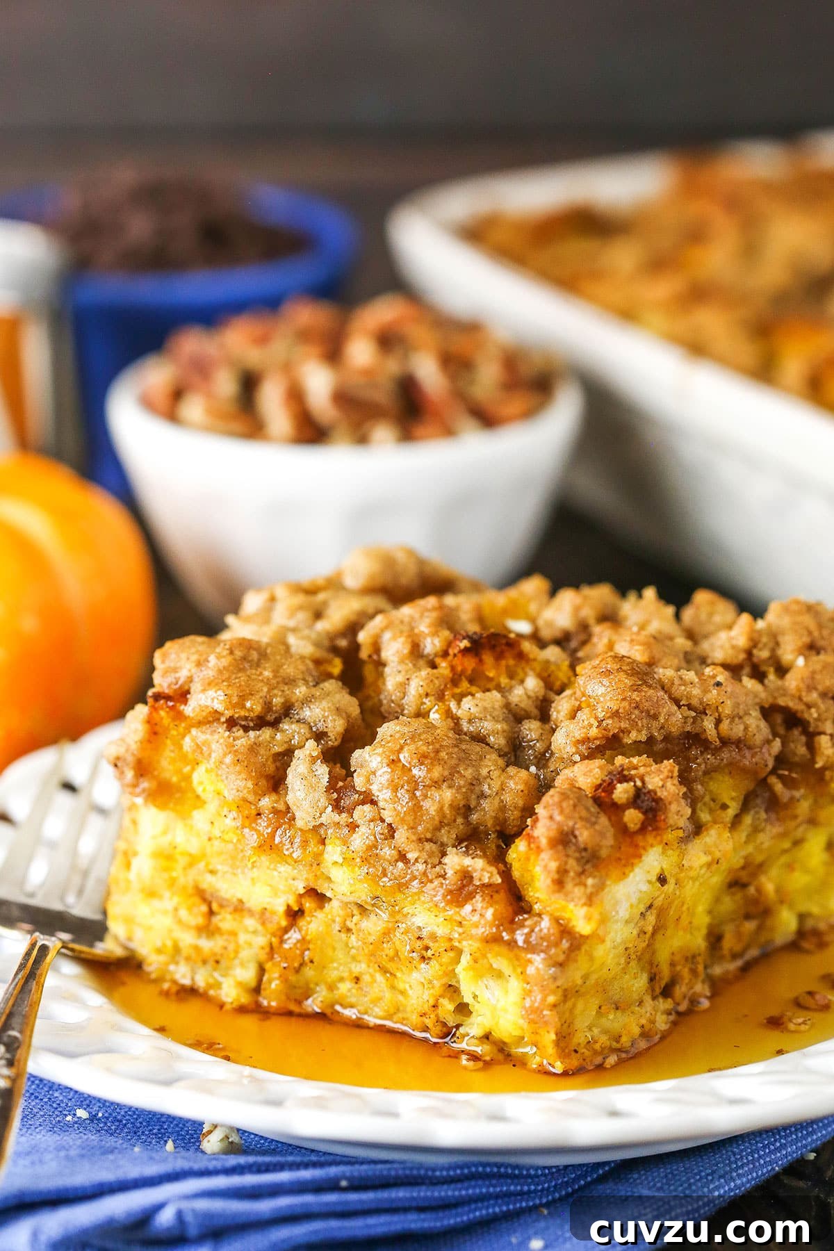 A tempting serving of Pumpkin French Toast Casserole, garnished beautifully. Side view of a square serving of Overnight Pumpkin French Toast Casserole on a white plate with a fork, ready for a delicious breakfast.