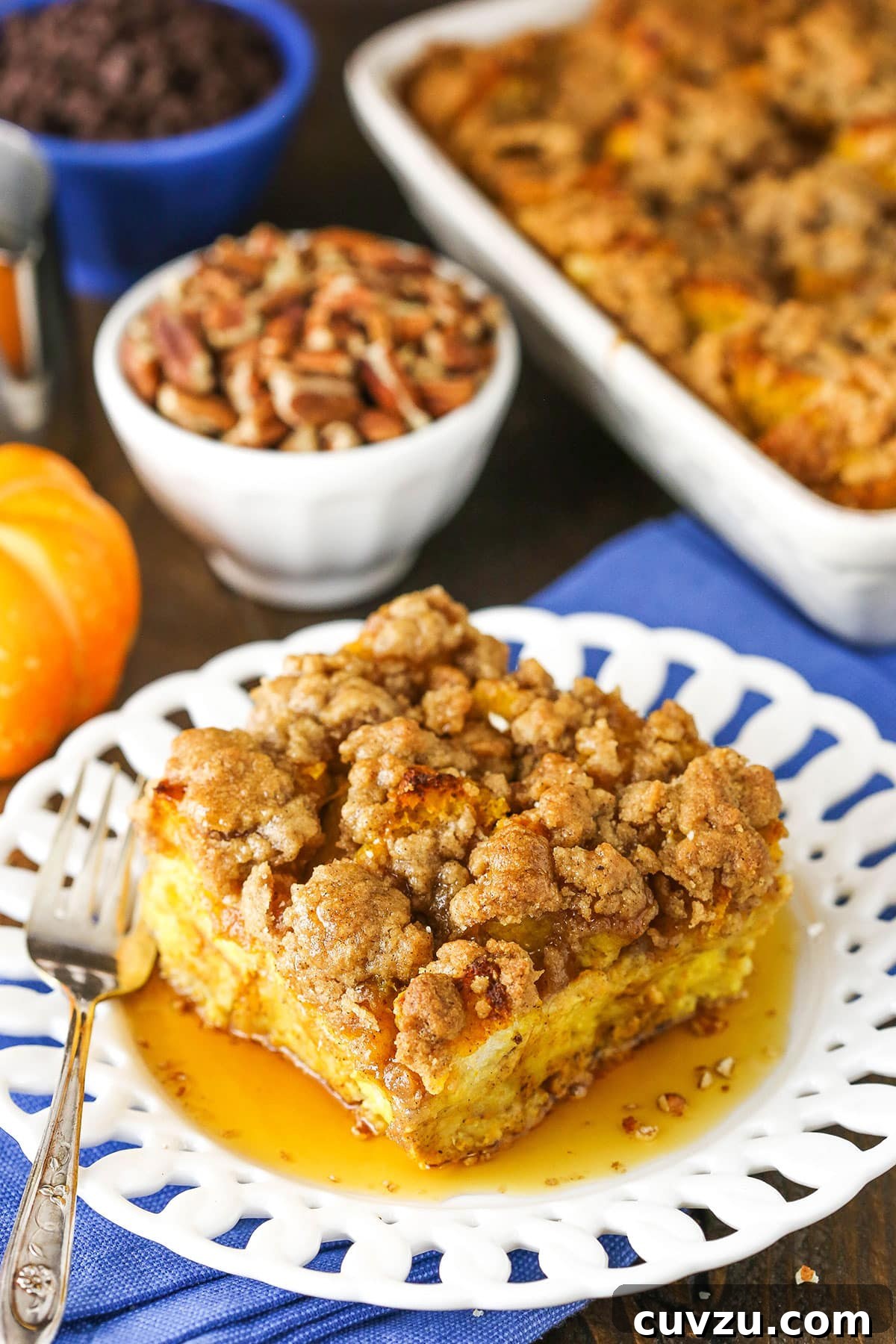 A beautifully plated serving of Pumpkin French Toast Casserole. Overhead view of a square serving of Overnight Pumpkin French Toast Casserole on a white plate with a fork, showcasing its streusel and golden-brown perfection.
