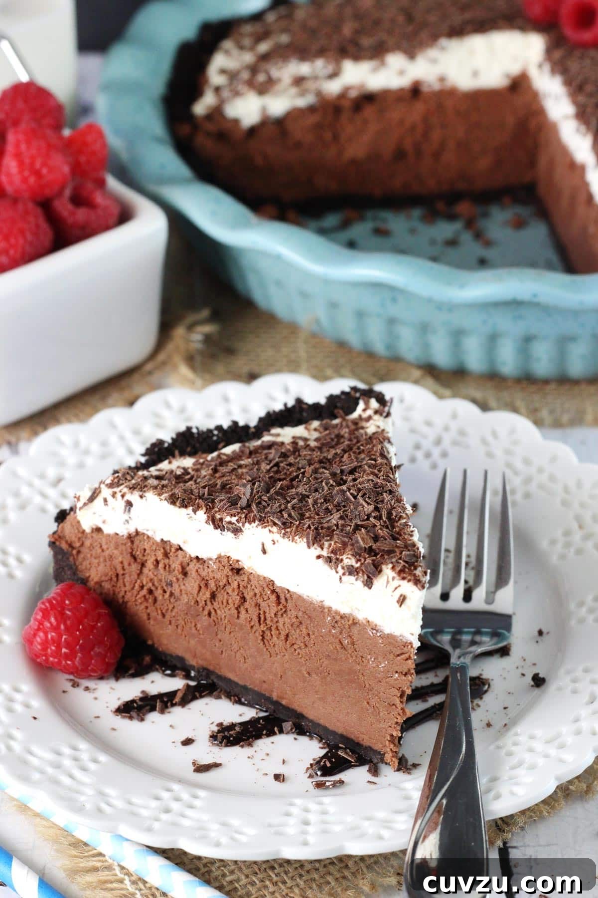 Decadent Chocolate Truffle Pie 2 A slice of chocolate truffle pie on a white plate with the rest of the pie in the background.