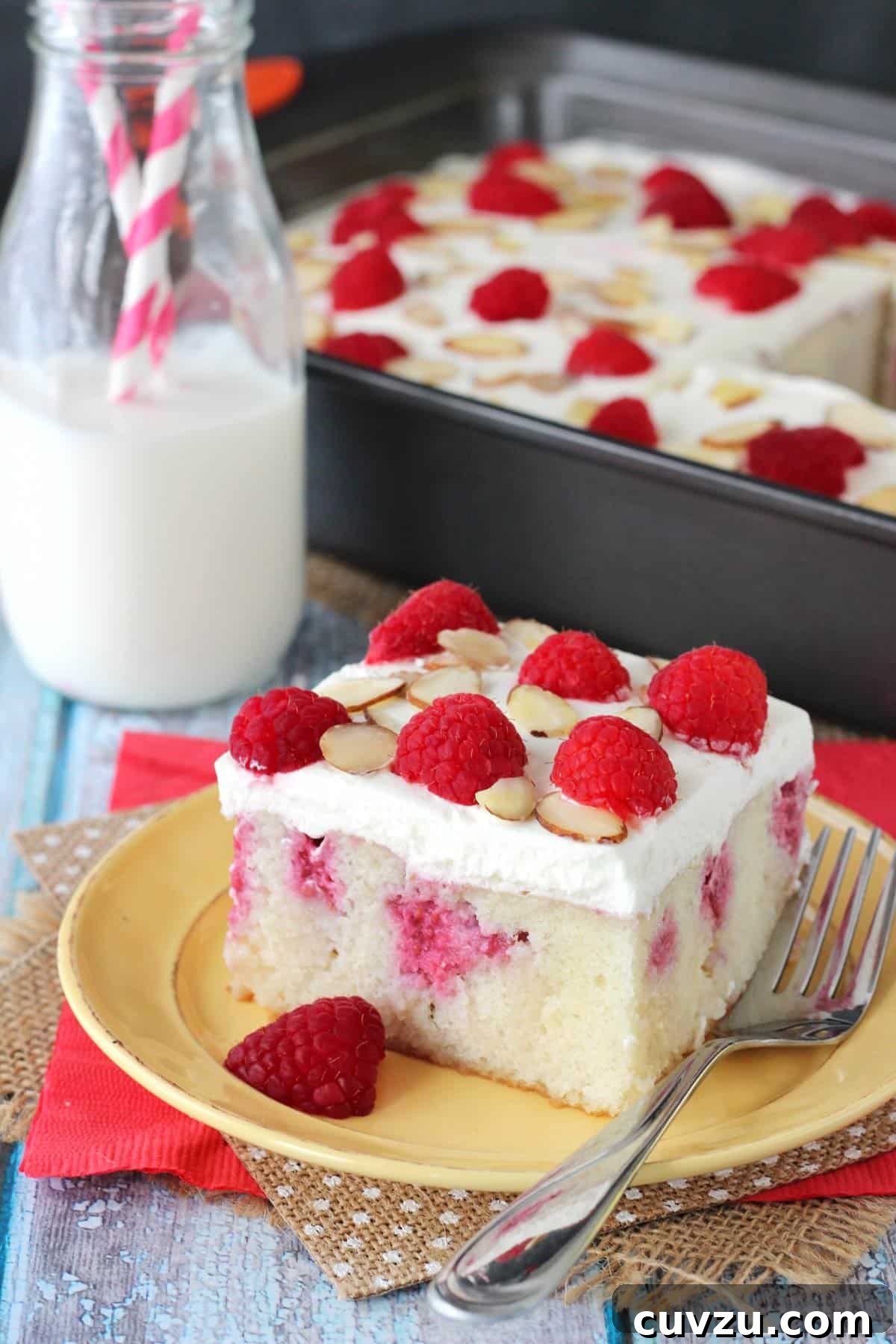 Raspberry Almond Infusion Cake 8 A vibrant and tempting full Raspberry Almond Poke Cake with fresh berries and almond slivers as garnish, viewed from above in its baking pan.