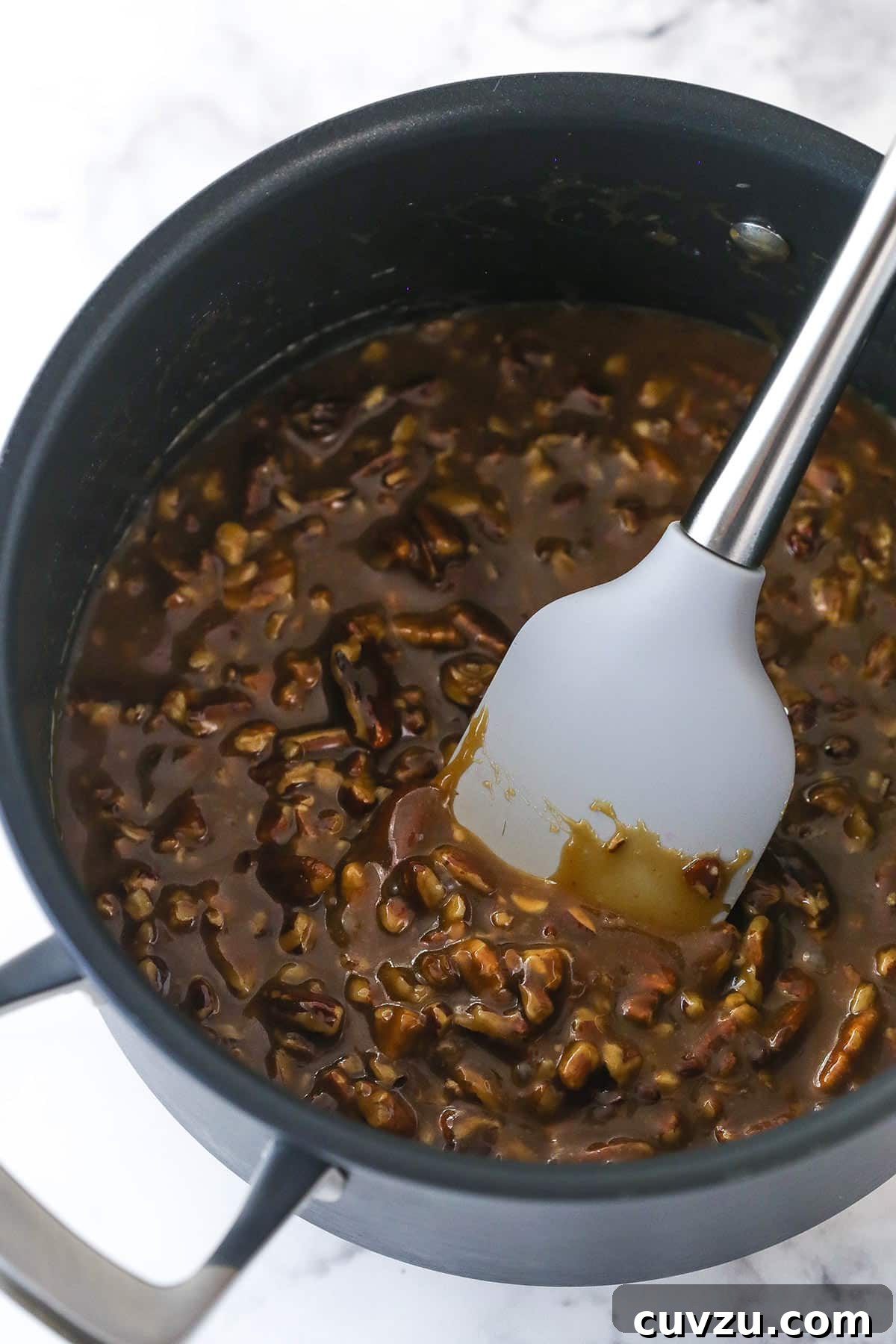 Pecan pie cheesecake combines all of the goodness of classic pecan pie with a smooth, creamy cinnamon cheesecake filling. Stirring ingredients for the pecan topping in a saucepan on the stovetop.