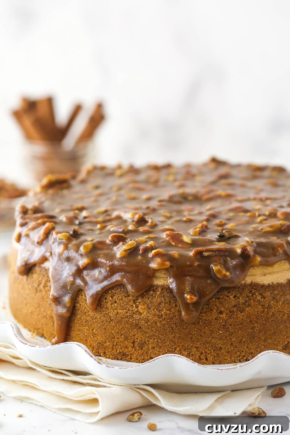 Pecan pie cheesecake combines all of the goodness of classic pecan pie with a smooth, creamy cinnamon cheesecake filling. A complete pecan pie cheesecake sitting on a serving platter, ready to be sliced.