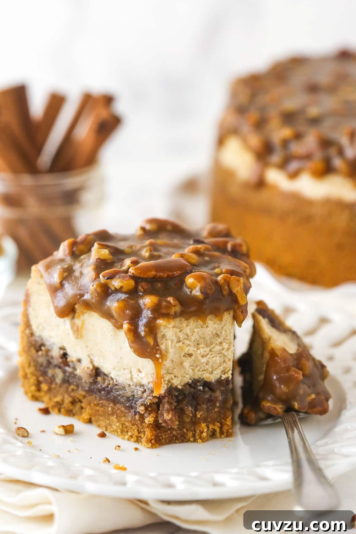 Pecan pie cheesecake combines all of the goodness of classic pecan pie with a smooth, creamy cinnamon cheesecake filling. A fork taking a bite out of a slice of pecan pie cheesecake, highlighting the gooey layers.
