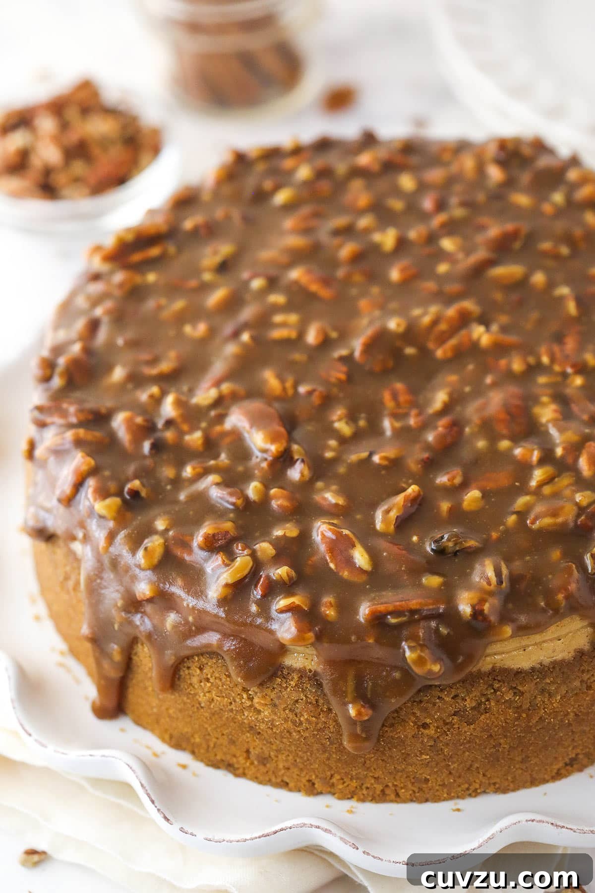 Pecan pie cheesecake combines all of the goodness of classic pecan pie with a smooth, creamy cinnamon cheesecake filling. Overhead view of a beautiful pecan pie cheesecake on a serving platter, garnished and ready.