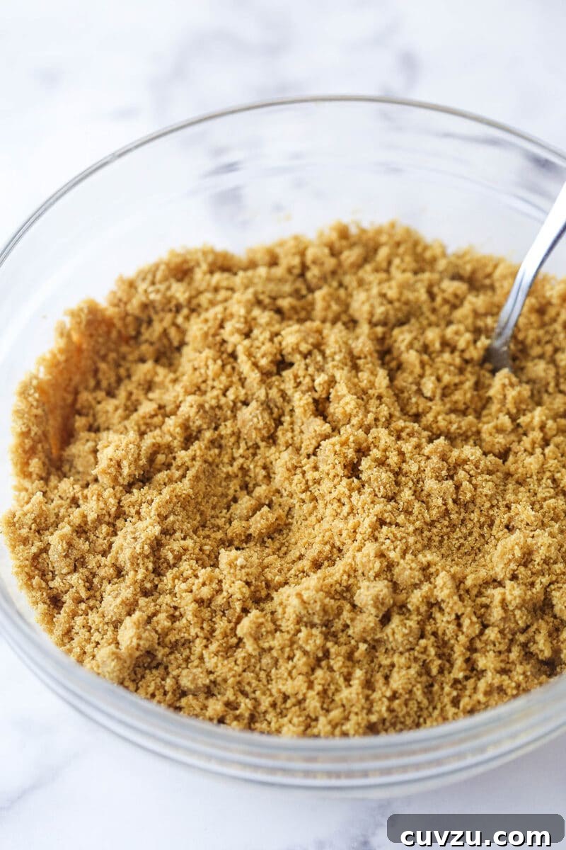 Pecan pie cheesecake combines all of the goodness of classic pecan pie with a smooth, creamy cinnamon cheesecake filling. Mixing together ingredients for a graham cracker crust in a bowl.
