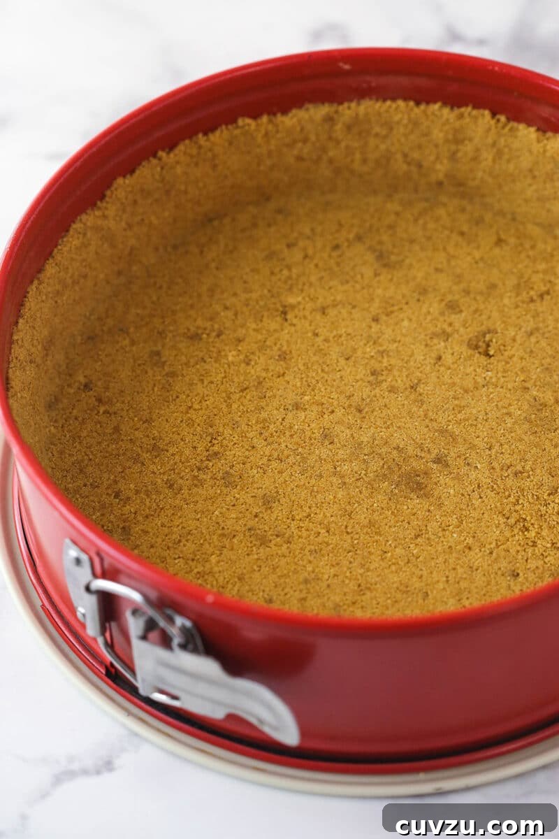 Pecan pie cheesecake combines all of the goodness of classic pecan pie with a smooth, creamy cinnamon cheesecake filling. Graham cracker crust evenly pressed into a springform pan, ready for baking.