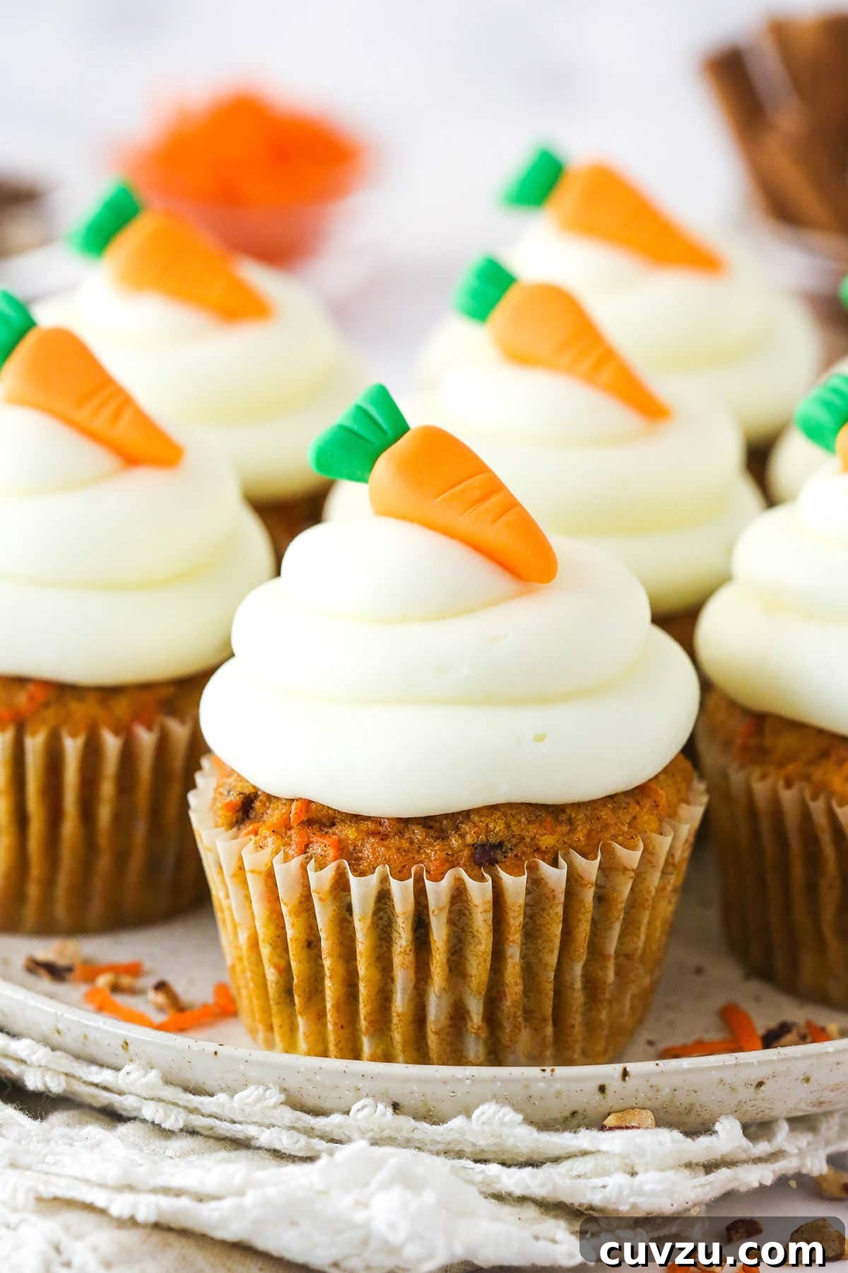 These moist carrot cake cupcakes are loaded with warm spices, teaming with exciting mix-ins, and topped with the best cream cheese frosting. Carrot cake cupcakes on a serving platter topped with mini carrot toppers.