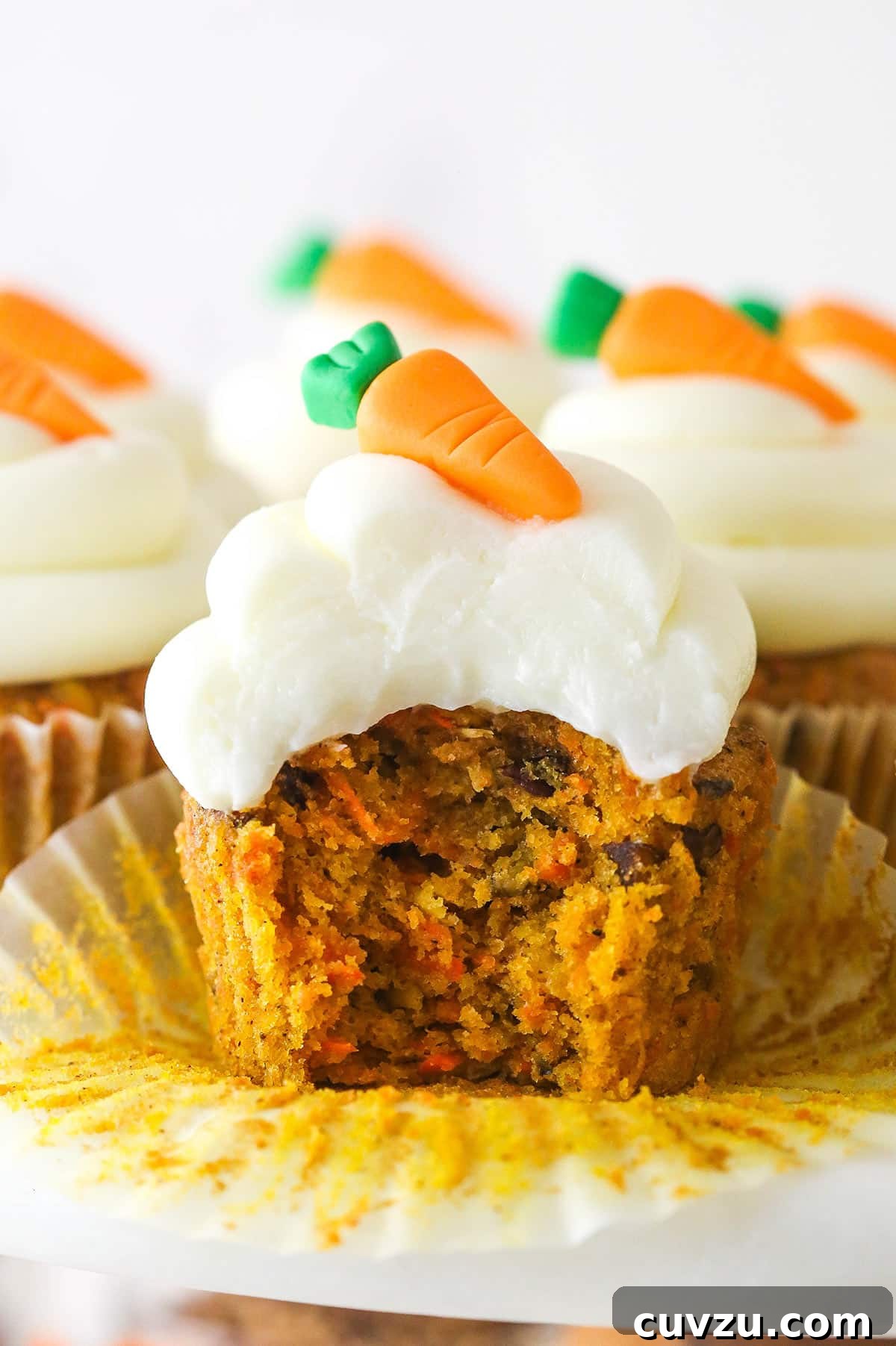 These moist carrot cake cupcakes are loaded with warm spices, teaming with exciting mix-ins, and topped with the best cream cheese frosting. A carrot cake cupcake with a bite taken out of it.