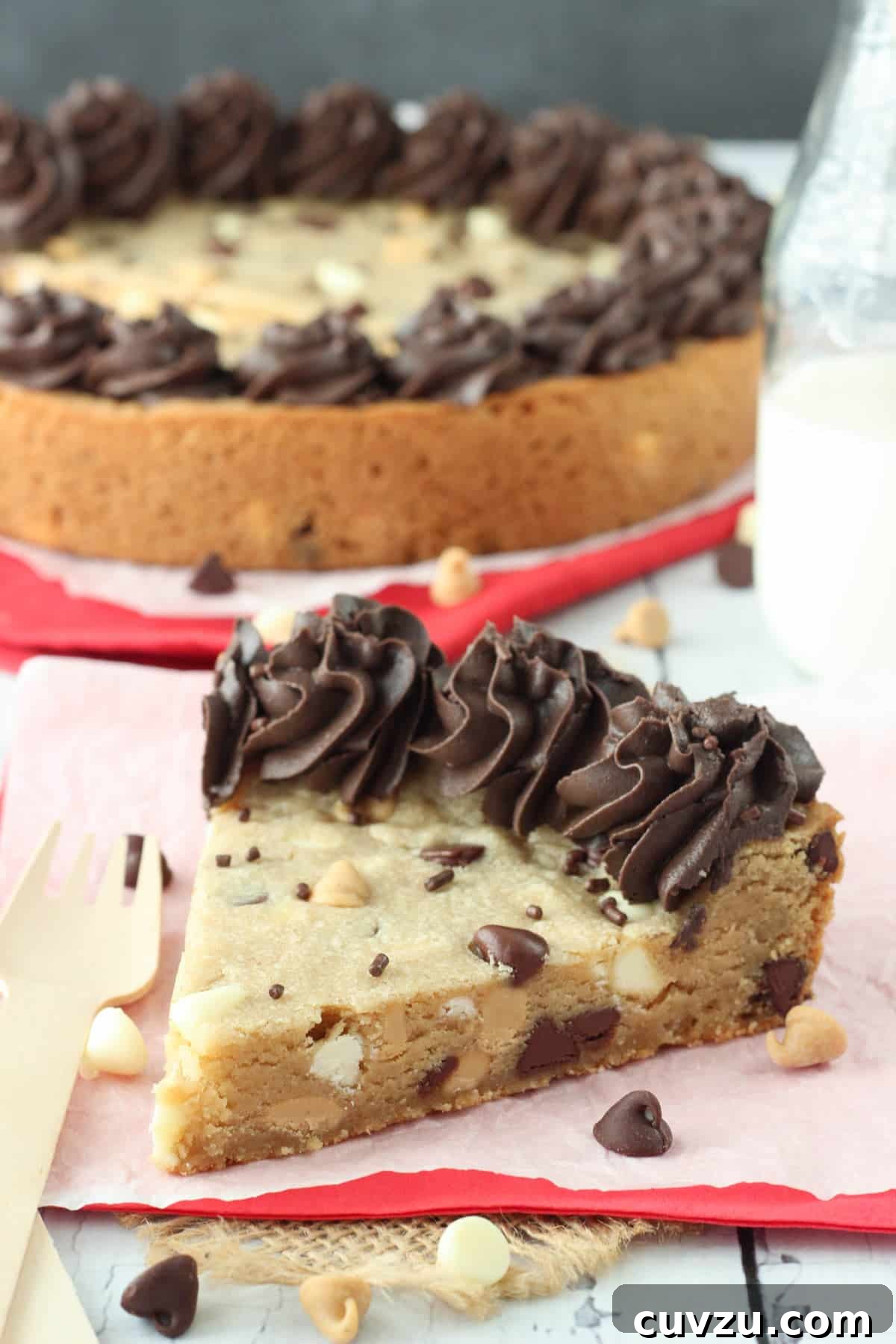 Ultimate Triple Chocolate Chip Cookie Cake 2 A generous slice of Triple Chocolate Chip Cookie Cake on a white plate, with the full decorated cake blurred in the background, showcasing its soft, chewy texture.