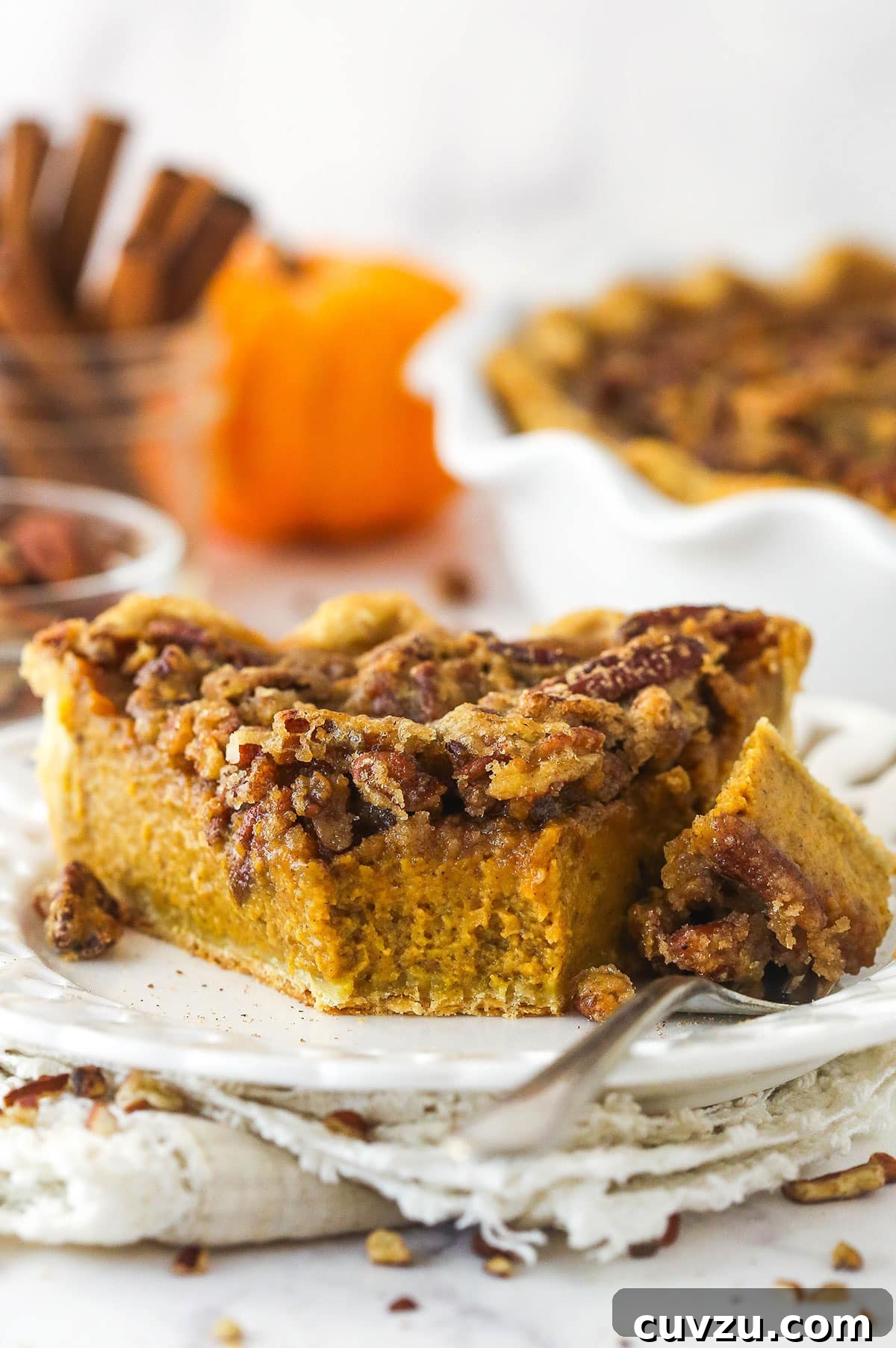 Caramelized Pecan Pumpkin Pie 4 A delectable slice of pecan praline pumpkin pie on a plate, with a fork holding a bite-sized portion.