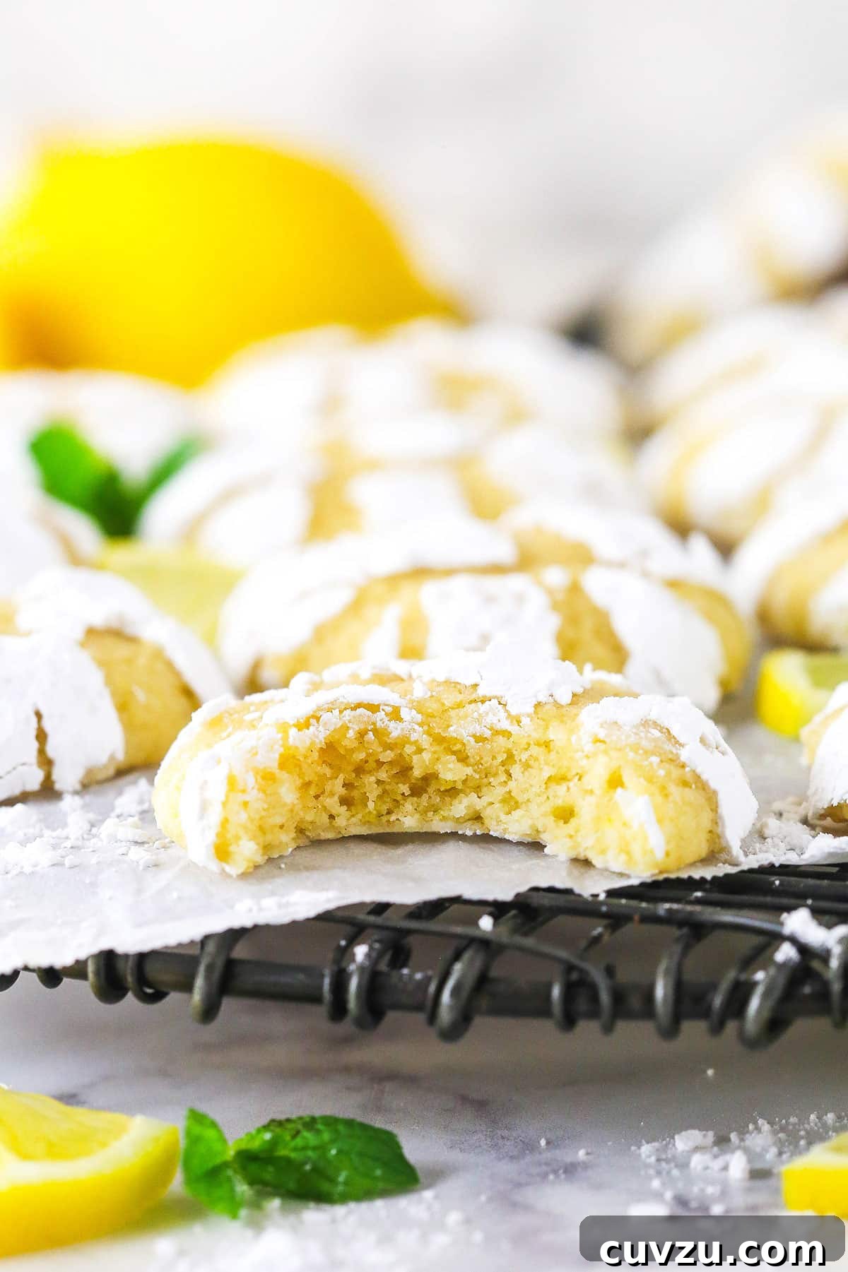 Indulge in the irresistible texture and flavor of these Lemon Crinkle Cookies, revealing a soft center and bright lemony taste with every bite. A close-up of a lemon crinkle cookie with a bite taken out, revealing its soft, chewy interior and vibrant lemon yellow color.