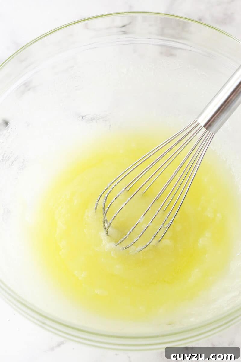Whisking together the foundational ingredients: melted butter and sugar for a perfectly sweet and tender Lemon Crinkle Cookie dough. The initial step of whisking together creamy melted butter and granulated sugar for the lemon crinkle cookie dough base.