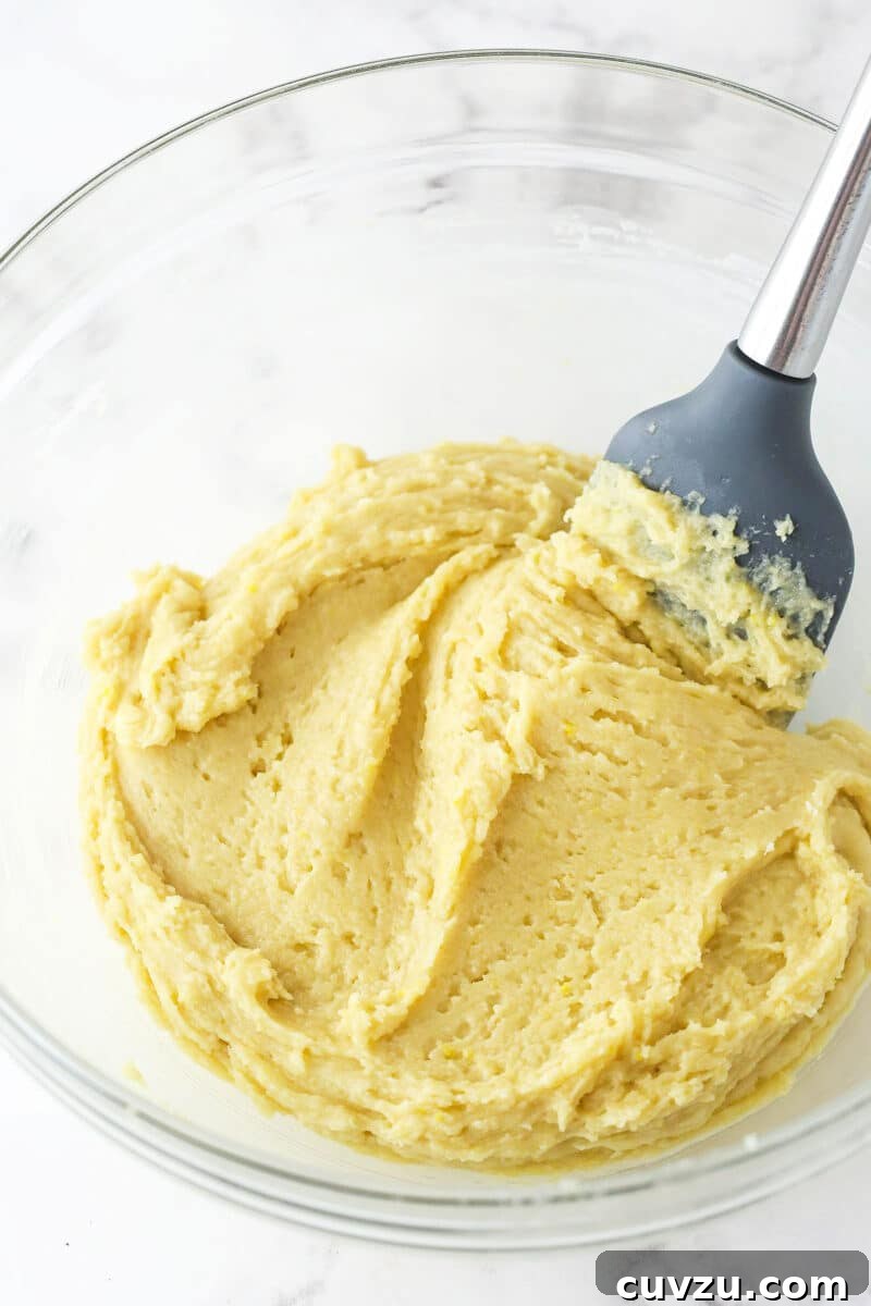 The crucial step of combining wet and dry ingredients for Lemon Crinkle Cookies, ensuring a tender and flavorful dough. Carefully mixing the dry flour mixture into the wet ingredients for lemon crinkle cookie dough, ensuring a perfectly combined yet not overmixed batter.