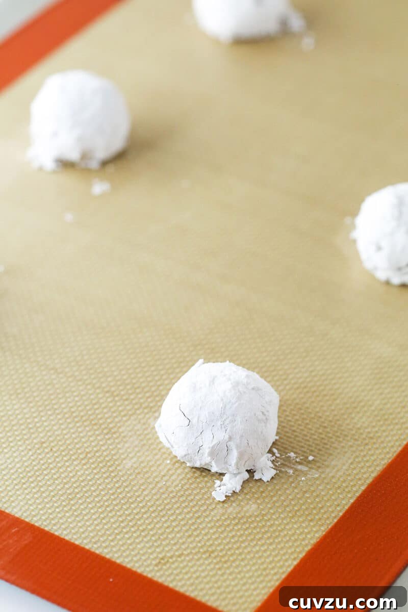 The essential second step: generously rolling cookie dough in powdered sugar for that classic crackle effect before baking. Lemon cookie dough balls meticulously coated in a thick layer of powdered sugar, poised and ready to be baked into crackled perfection.