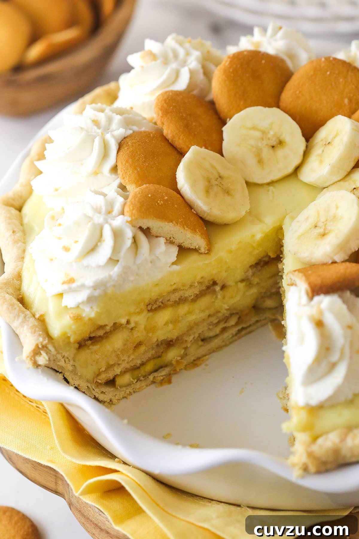 A stunning banana pudding pie, showcasing its perfect layers of fresh bananas, crunchy Nilla wafers, and luscious pudding, crowned with whipped cream. A beautifully presented banana pudding pie with a slice missing, revealing the delightful layers of banana, Nilla wafers, and creamy pudding.