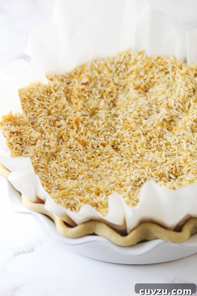 Blind baking the pie crust, weighed down with rice to prevent shrinking. A pie crust lined with parchment paper and filled with pie weights (rice), prepared for blind baking.