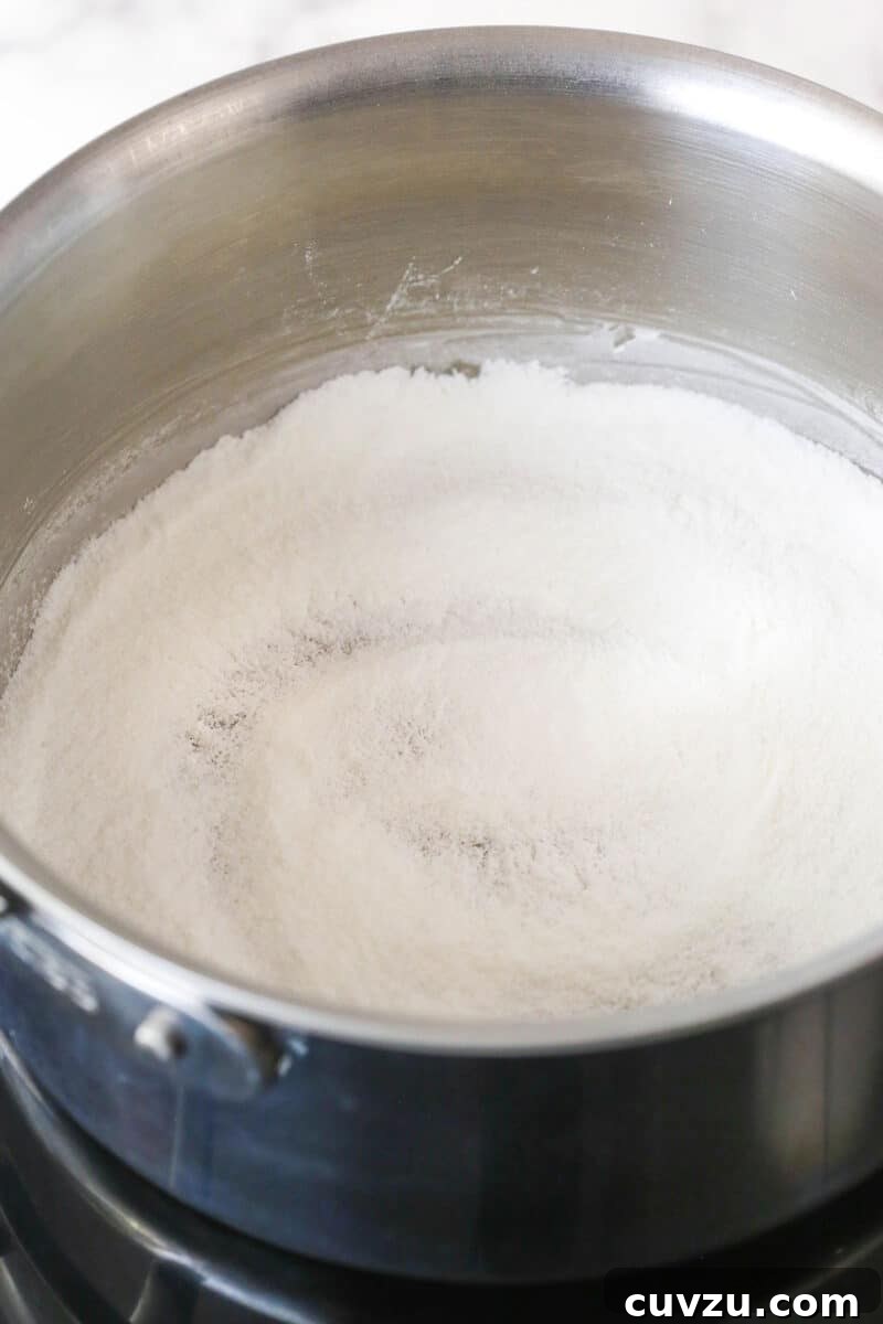 The dry ingredients for the pudding (sugar, cornstarch, and salt) in a saucepan. Granulated sugar, cornstarch, and salt whisked together in a saucepan before liquids are added for the pudding.