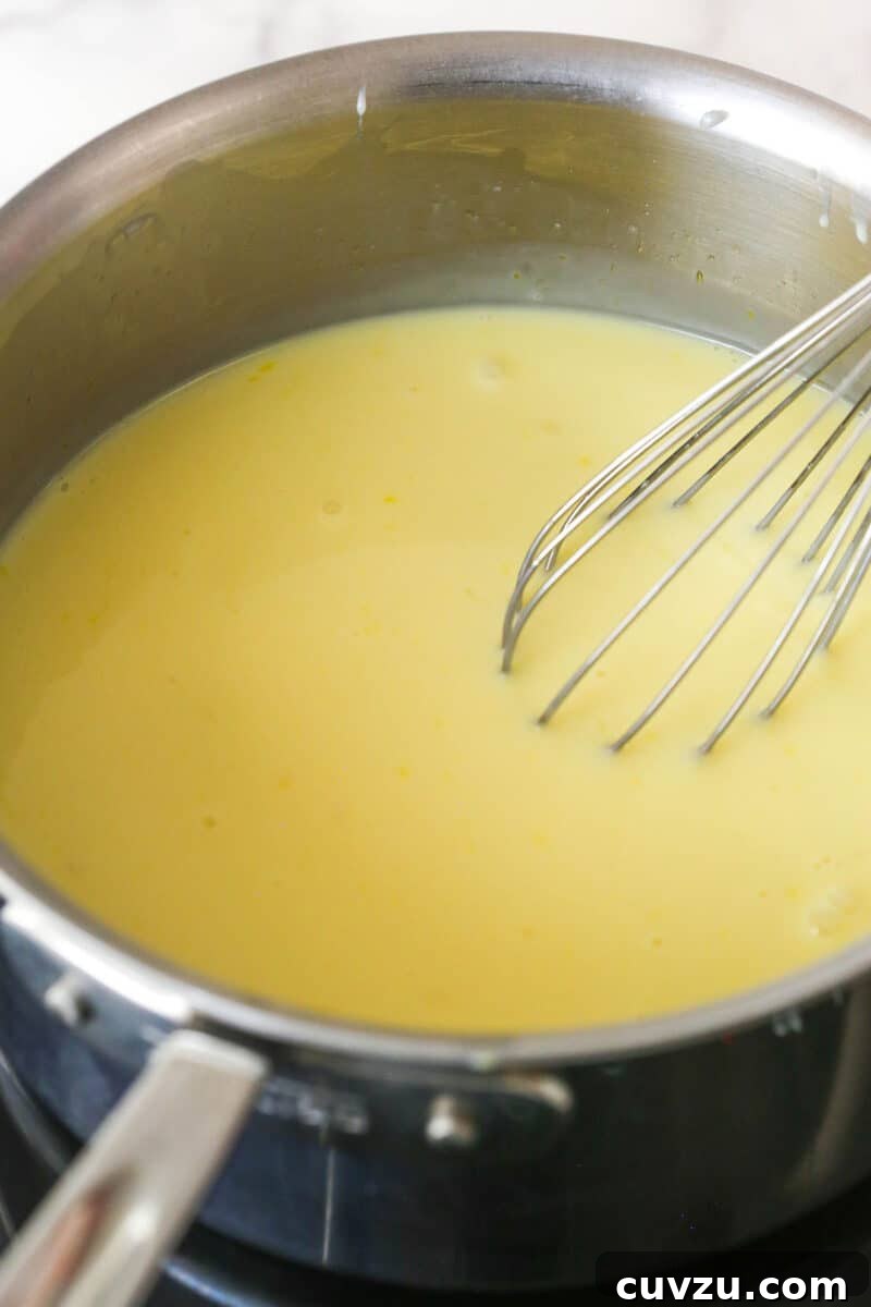 Whisking the wet ingredients (milk, sweetened condensed milk, eggs) into the dry mix for the pudding. Milk, sweetened condensed milk, and eggs being whisked into the dry ingredients in a saucepan for the pudding.