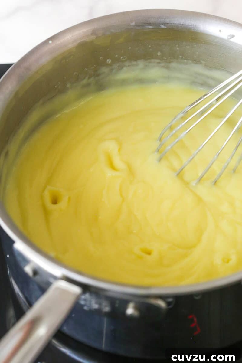 The pudding mixture thickening on the stovetop, being continuously whisked. The pudding mixture being constantly whisked over medium-low heat in a saucepan as it thickens.