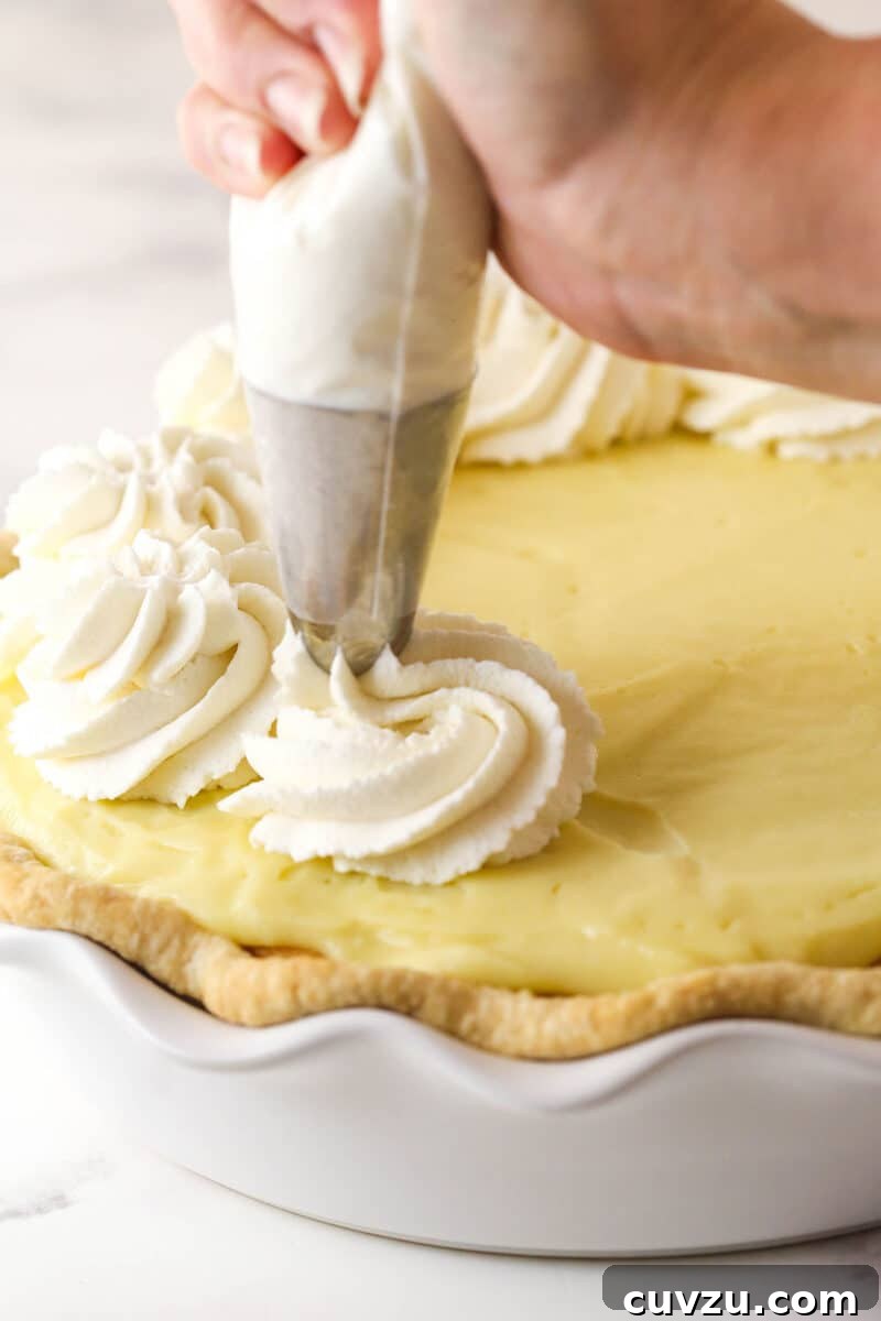Piping fluffy whipped cream onto the chilled banana pudding pie, adding a beautiful final touch. Whipped cream being piped decoratively onto the top of a chilled banana pudding pie using a piping bag.
