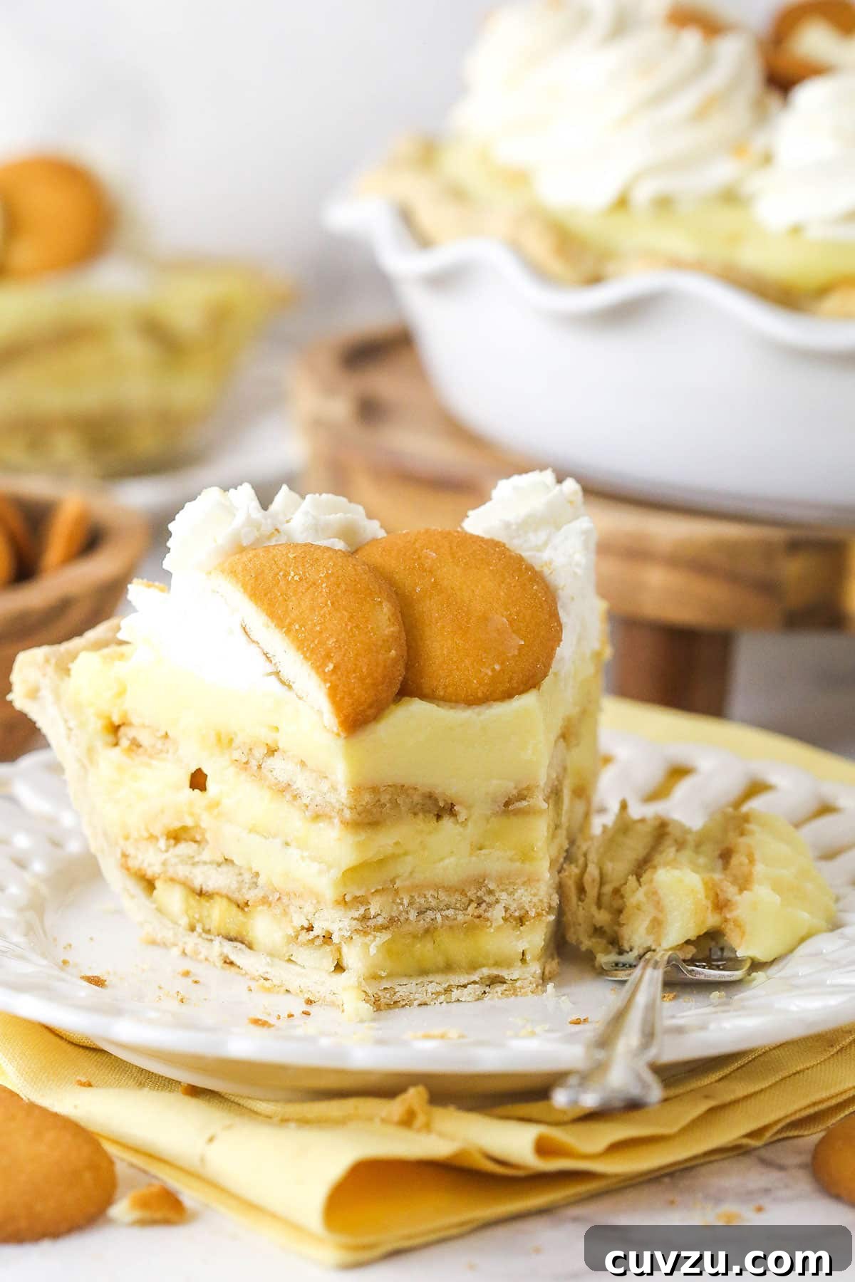 A tantalizing slice of banana pudding pie, revealing its delicious layers and a creamy, inviting texture. A delicious slice of banana pudding pie with a bite taken out, highlighting the creamy texture and layers.
