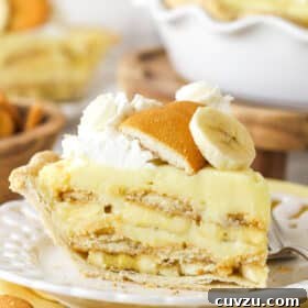 Side view of a perfectly sliced banana pudding pie on a white plate, revealing its creamy layers.