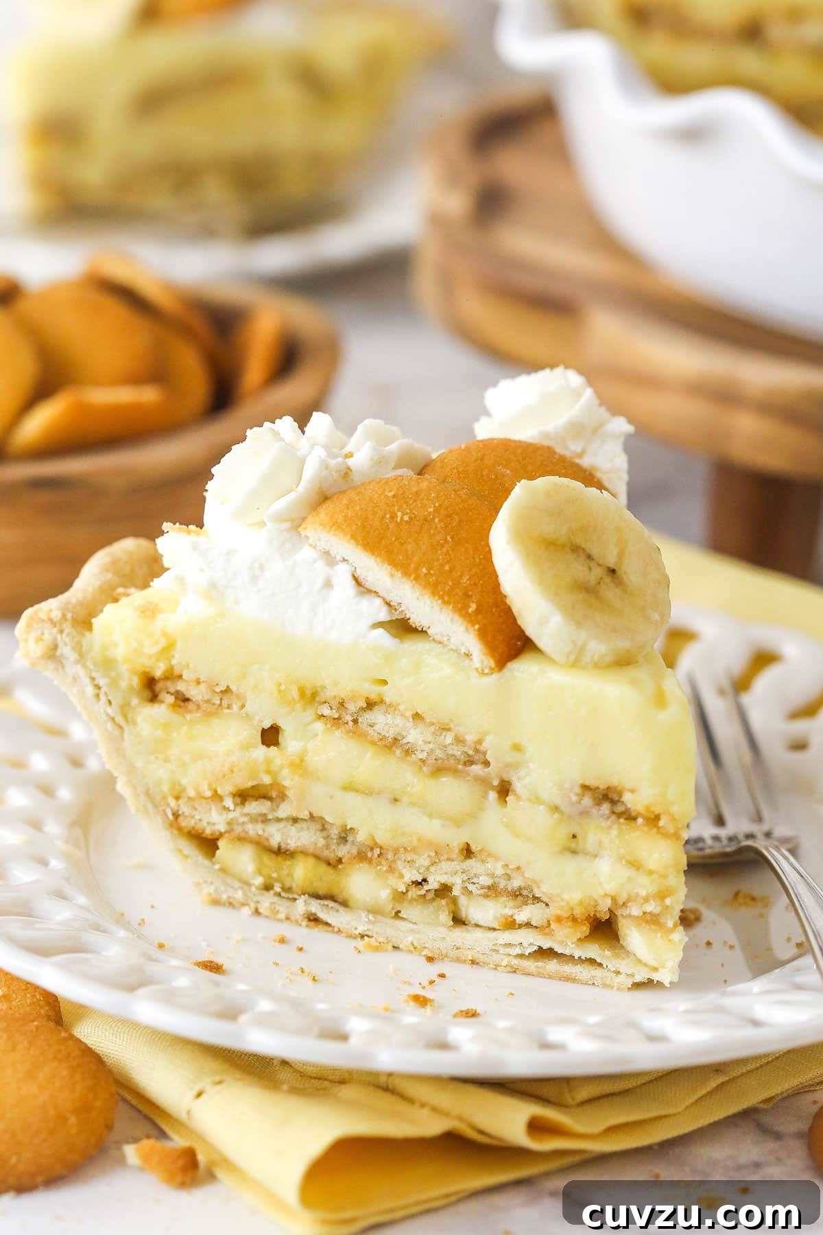 A tempting slice of banana pudding pie, featuring layers of bananas, Nilla wafers, pudding, and whipped cream, on a white plate. A pristine slice of banana pudding pie, expertly plated on a white dish, ready to be enjoyed.
