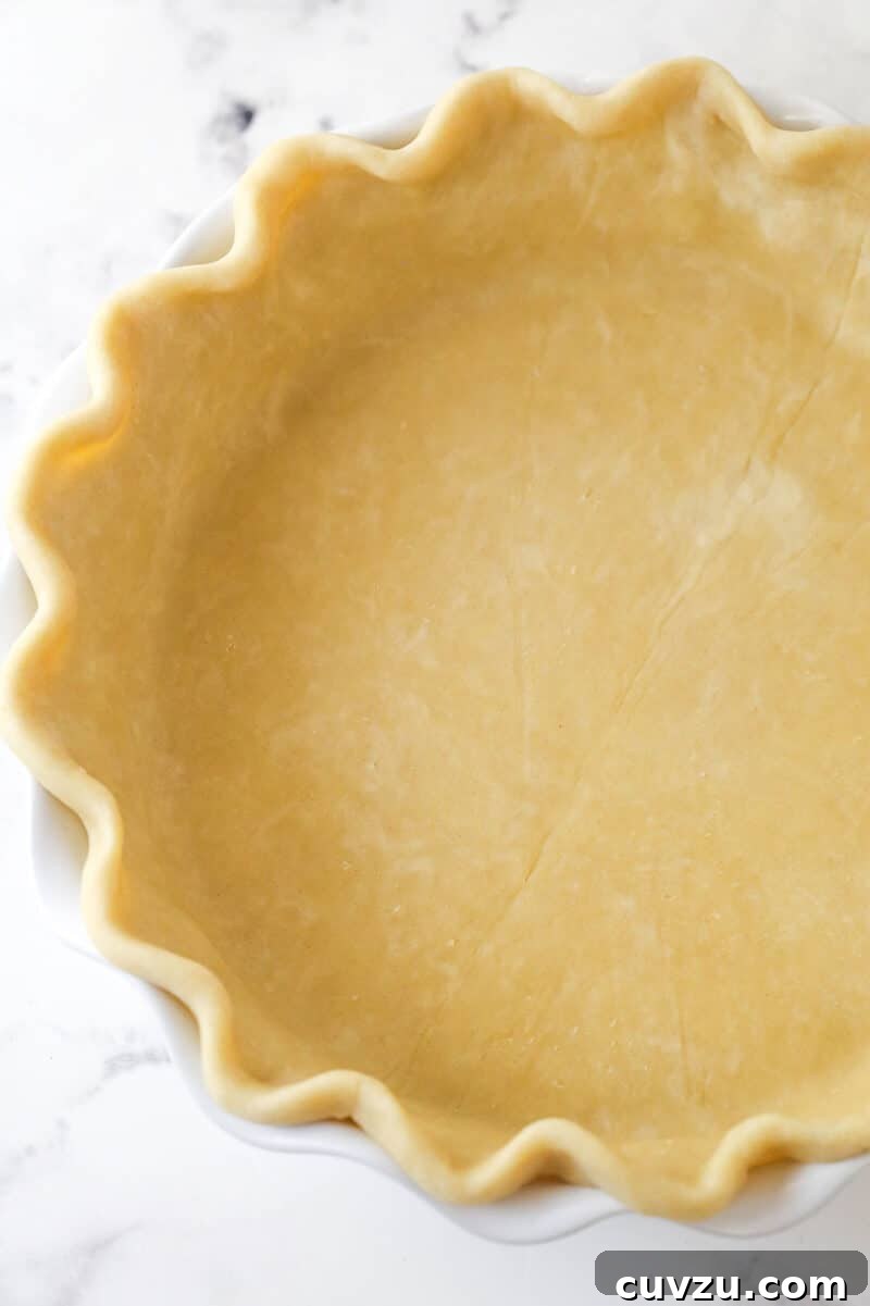 The pie crust artfully placed and crimped in a pie dish, anticipating its delicious filling. A homemade pie crust meticulously shaped and docked in a pie pan, ready for blind baking.