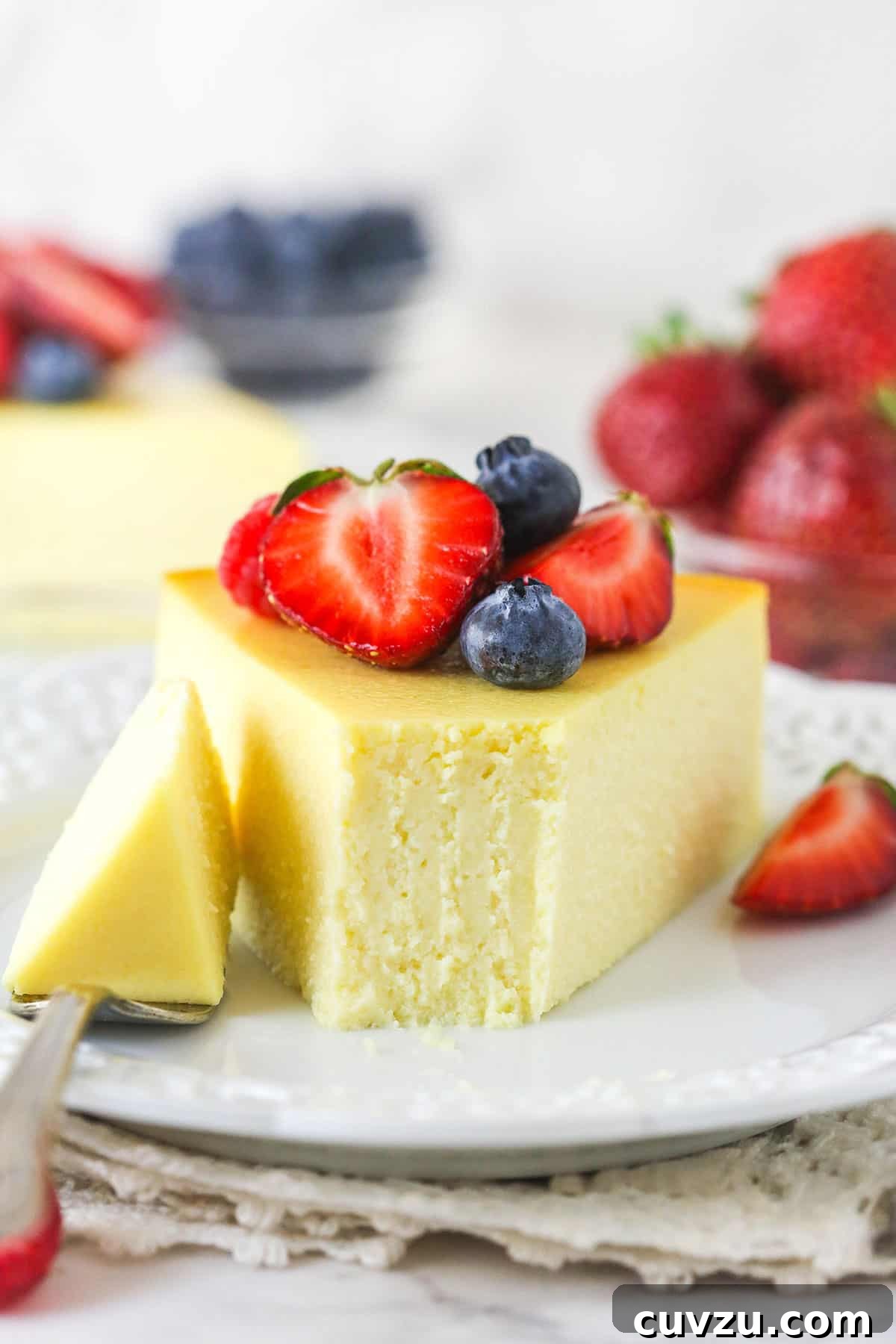 Ricotta Cheesecake Slice with Fork Bite A close-up shot of a slice of ricotta cheesecake on a plate, with a fork holding a bite-sized piece next to it, emphasizing its light, airy texture.