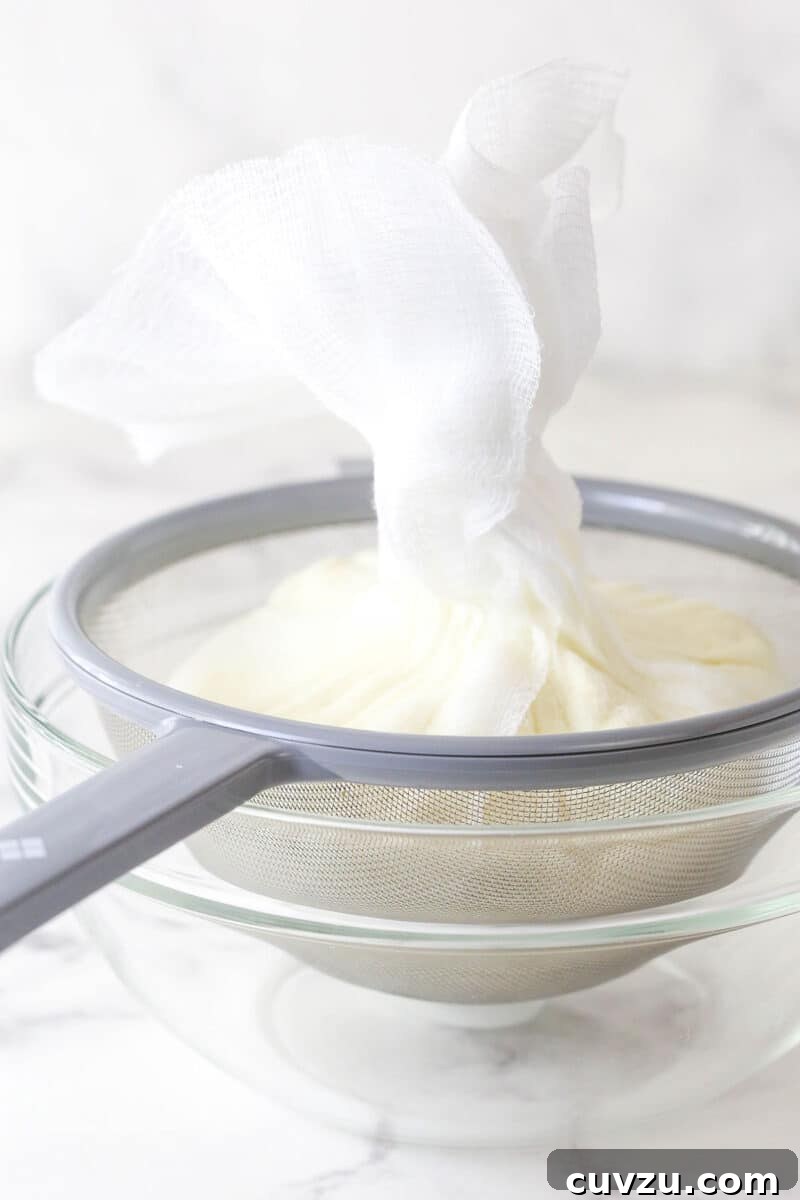 Straining Ricotta Cheese for Cheesecake Close-up shot of ricotta cheese being strained through cheesecloth in a fine-mesh strainer over a bowl.