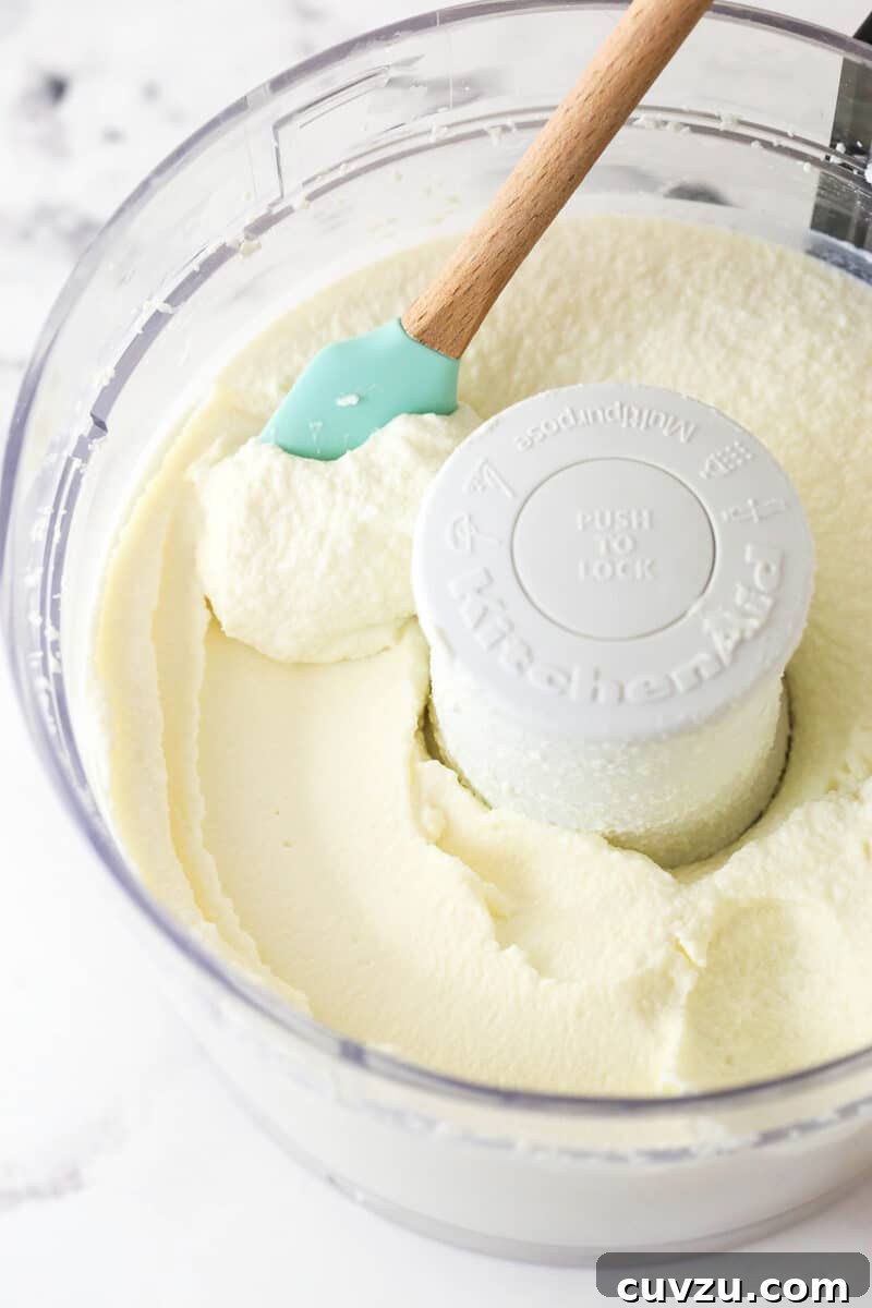 Processing Ricotta for Smooth Cheesecake Filling Strained ricotta cheese being processed in a food processor until smooth and creamy.