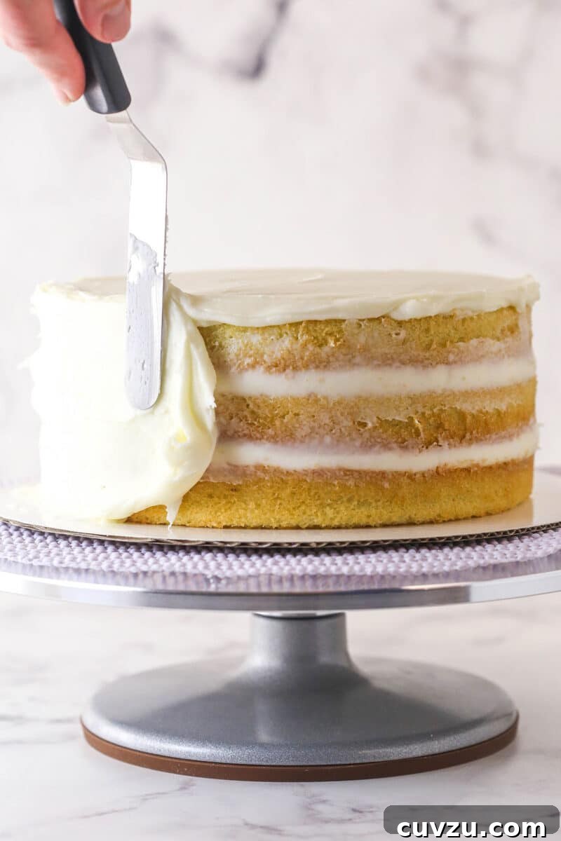 Tropical Delight Cake 13 A layered coconut cake on a turntable, with buttercream being spread smoothly onto its side.
