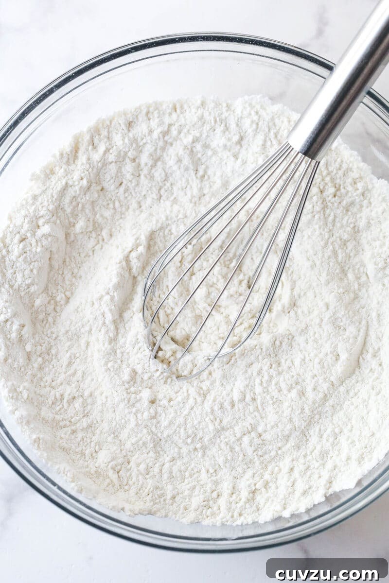 Tropical Delight Cake 6 Dry ingredients combined in a clear glass bowl, showcasing the flour, baking powder, baking soda, and salt.